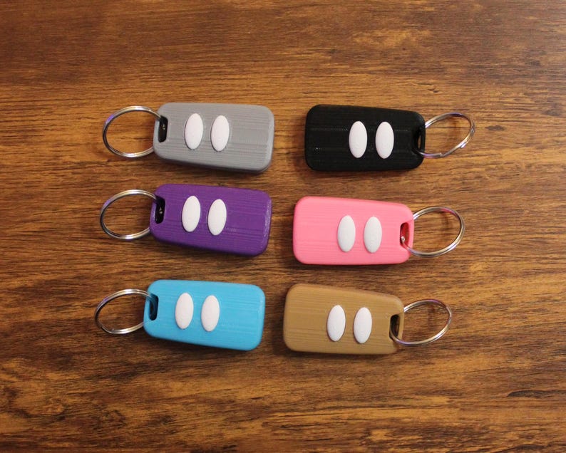 May include: Six keychains with different colored plastic key fob cases. Each keychain has a silver ring and two white buttons. The colors of the key fobs are gray, black, purple, pink, blue, and brown.