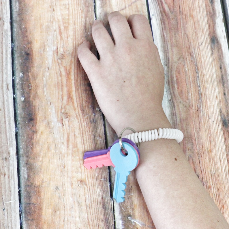 May include: A white coiled key chain bracelet with a set of colorful plastic keys attached. The keys are pink, purple, and blue.