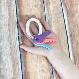 May include: A white coiled key chain with three plastic keys attached. The keys are purple, pink, and blue.