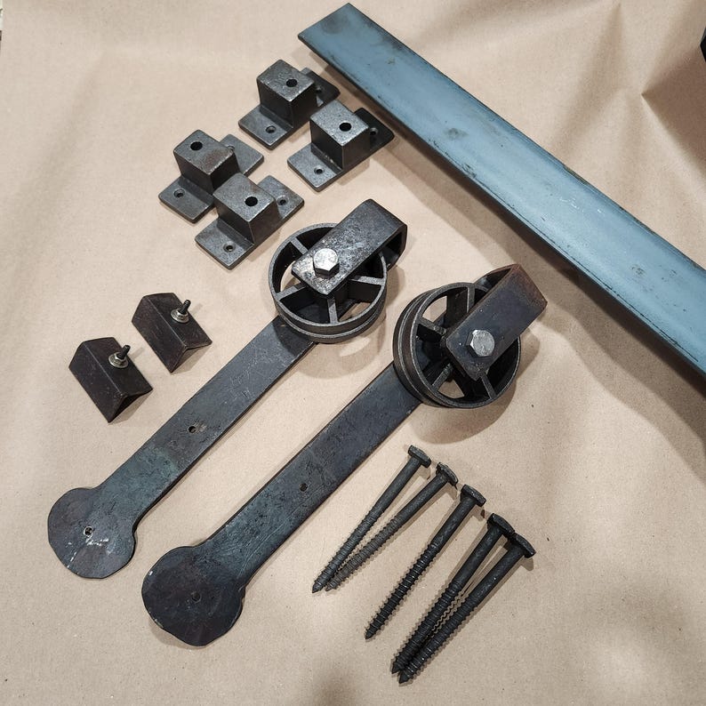 May include: A set of black metal hardware for a sliding barn door. The set includes two black metal door rollers, two black metal door hangers, four black metal mounting brackets, and eight black screws.