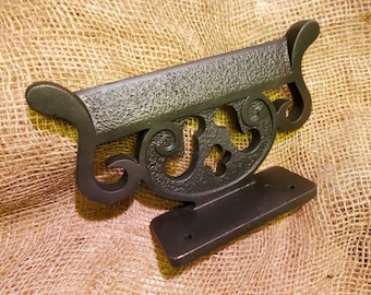 May include: Black metal wall mount with a decorative scroll design. The mount has a flat surface for attaching a sign or plaque.