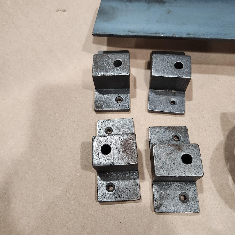 May include: Four metal brackets with a rough, aged finish. Each bracket has a square shape with a round hole in the center and three smaller holes around the edges.