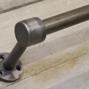 May include: A close-up of a black metal handrail with a round end cap and a flat base plate. The handrail is mounted to a wall.