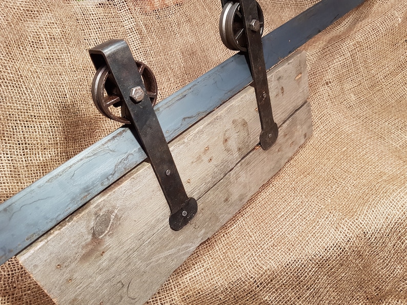 May include: A rustic wooden door with a metal sliding track and two black metal wheels. The door is mounted on a burlap background.