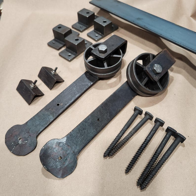 May include: A set of black metal barn door hardware, including two sliding door rollers, two door brackets, and six screws. The rollers have a circular design with a central spoke and a decorative edge.
