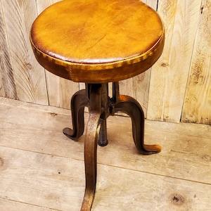 May include: A brown leather-covered stool with a metal base and three legs. The stool is adjustable in height.