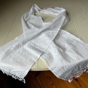 May include: White cotton scarf with a delicate embroidered design and a fringed edge.