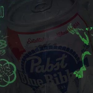 May include: A green glow-in-the-dark sticker of a monster with a single eye and sharp teeth. The sticker is placed on a can of Pabst Blue Ribbon beer. The can is silver with a red and blue label. The text "Established Milwaukee 1844" is visible on the label.