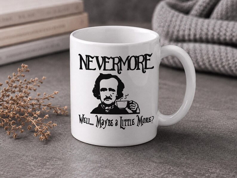 May include: A white ceramic mug featuring a black graphic illustration of Edgar Allan Poe holding a small cup. The text "NEVERMORE" is printed above the illustration, and the text "Well... Maybe a Little More?" is printed below the illustration.