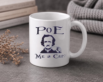 May include: White ceramic mug with a dark blue illustration of Edgar Allan Poe holding a teacup, with the text "PoE Me a Cup?" in dark blue. The mug has a curved handle and is set against a neutral background.