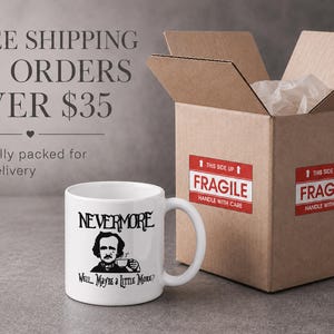 May include: A white ceramic mug featuring a black graphic illustration of Edgar Allan Poe holding a small cup. The text above the illustration reads NEVERMORE, and the text below reads Well... Maybe a Little More? The mug has a standard handle.