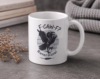 May include: White ceramic mug featuring a black raven illustration with the text "F-CAW-F? Nevermore!" The raven is depicted with outstretched wings in front of a bookshelf. A feather graphic is below the text. The mug has a curved handle.