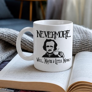 May include: A white ceramic mug featuring a black graphic illustration of Edgar Allan Poe holding a small teacup. The text NEVERMORE is printed above the portrait, and the text WELL... MAYBE A LITTLE MORE? is printed below the illustration.