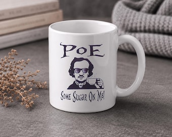 May include: White ceramic mug with a black and white illustration of Edgar Allan Poe wearing sunglasses and holding a teacup. The mug has the word "POE" above the illustration and the phrase "Some Sugar On Me!" below.