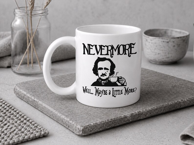 May include: A white ceramic mug featuring a black graphic illustration of Edgar Allan Poe holding a teacup. The text above the illustration reads NEVERMORE, and the text below reads Well... Maybe a Little More? The mug has a curved handle.