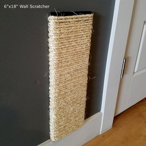 May include: A 6" x 18" wall-mounted cat scratching post made of natural sisal rope. The post is mounted on a gray wall with white trim.
