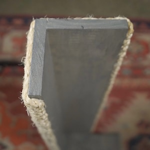 Op de afbeelding: Een close-up van een grijs houten plank met een natuurlijke touwrand. De plank is schuin en de touwrand is aan beide kanten zichtbaar.