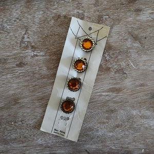 May include: Four amber glass buttons with gold metal trim on a white card with the text "Bee Hive Austria" printed on the bottom.