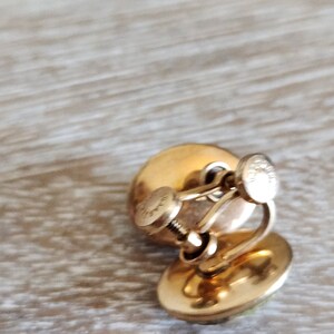 May include: A pair of gold tone clip-on earrings with a green stone in the center. The earrings have a screw-back closure.