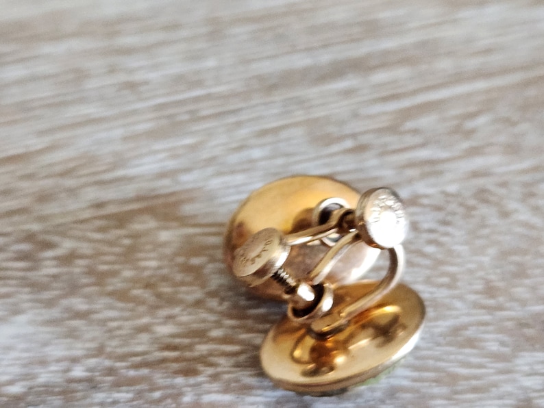 May include: A pair of gold tone clip-on earrings with a green stone in the center. The earrings have a screw-back closure.