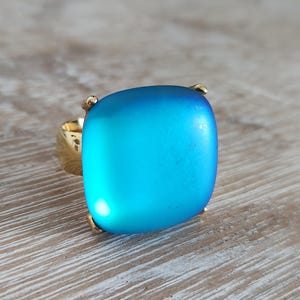 May include: A gold ring with a large, square, frosted blue gemstone.