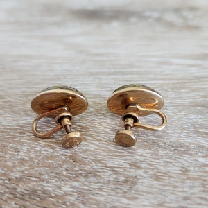 May include: A pair of gold tone clip-on earrings with green and white cameo-like designs.