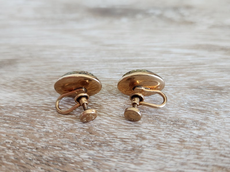 May include: A pair of gold tone clip-on earrings with green and white cameo-like designs.