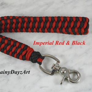 May include: A wrist lanyard crafted from black and red paracord in a braided pattern, featuring a silver-toned metal swivel lobster clasp. The text Imperial Red & Black and RainyDayzArt is printed in red and black on the surface.