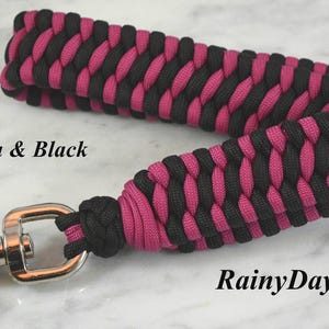 May include: A wrist lanyard crafted from magenta and black paracord in a braided pattern, featuring a silver-toned metal swivel lobster clasp. The text Magenta & Black and RainyDayzArt is printed on the image in a black serif font.