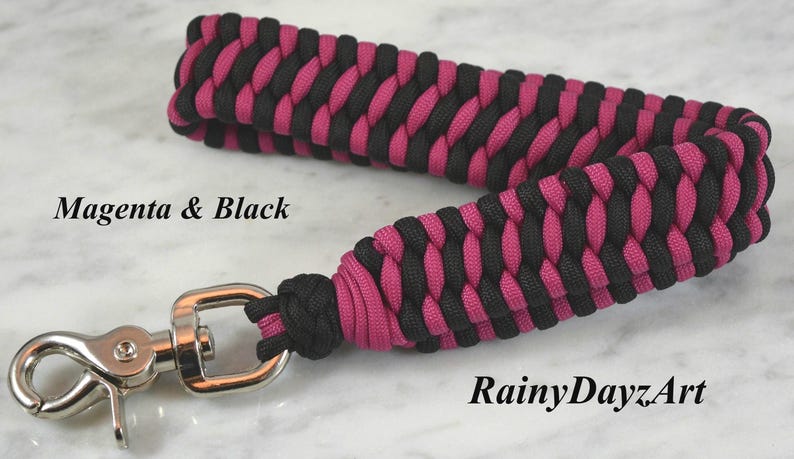 May include: A wrist lanyard crafted from magenta and black paracord in a braided pattern, featuring a silver-toned metal swivel lobster clasp. The text Magenta & Black and RainyDayzArt is printed on the image in a black serif font.