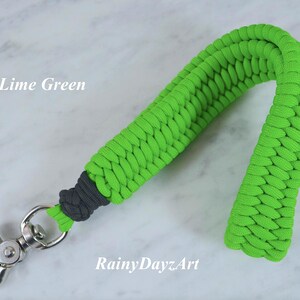 May include: A lime green paracord wrist lanyard featuring a braided pattern, a dark gray knot detail near the base, and a silver-toned metal swivel lobster clasp. The text "Lime Green" and "RainyDayzArt" are visible on the image.