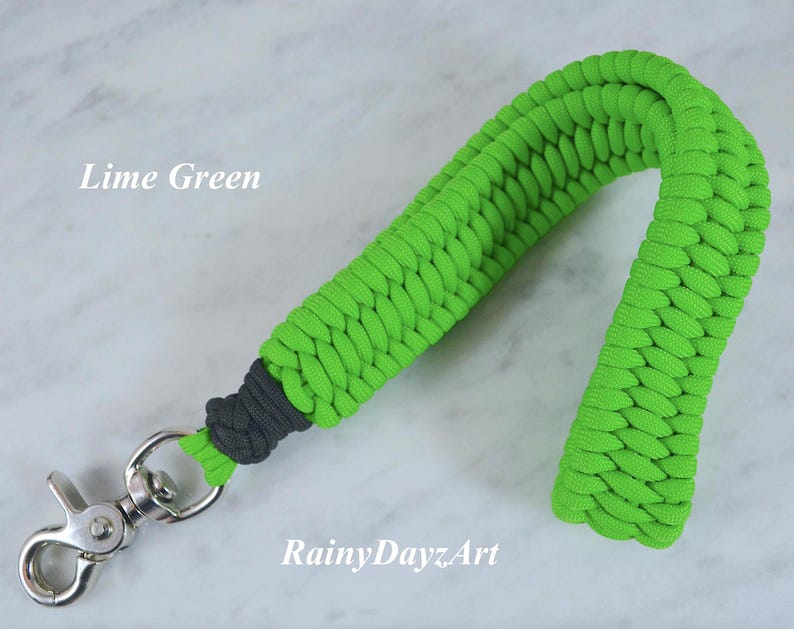 May include: A lime green paracord wrist lanyard featuring a braided pattern, a dark gray knot detail near the base, and a silver-toned metal swivel lobster clasp. The text "Lime Green" and "RainyDayzArt" are visible on the image.