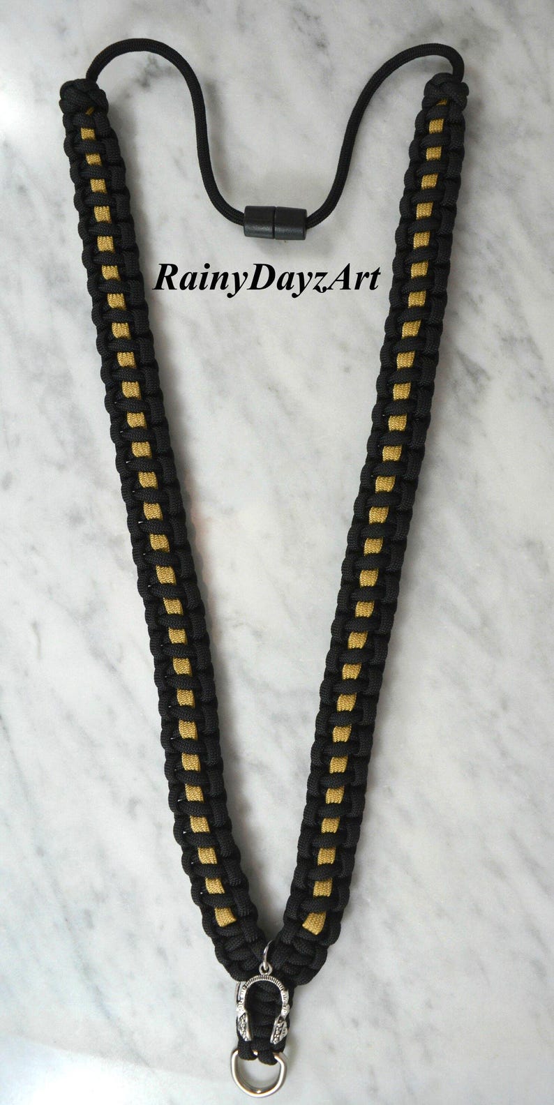 May include: Black and gold lanyard with a woven design. The lanyard has a black cord with gold accents and a black clasp. The text "RainyDayzArt" is visible on the image.
