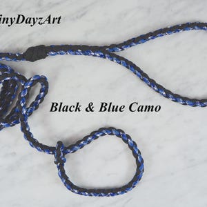 May include: A black and blue camo rope leash with a loop handle and a smaller loop at the end. The leash is made of braided rope and features the text "Black & Blue Camo" in black. The brand name "RainyDayzArt" is in the top left corner.