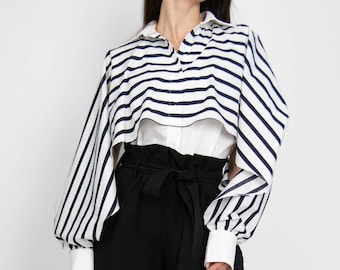 May include: A woman wearing a white and navy striped shirt with a black belt and black wide-leg trousers. She is wearing black sunglasses.