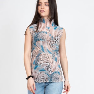 Könnte beinhalten: Ärmelloses Oberteil mit hohem Kragen, mit einem abstrakten Muster in Blau, Braun und Weiß. Kombiniert mit hellblauen Jeans und Zebra-Print-Absätzen. Das Outfit ist vor einem weißen Hintergrund.