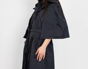 May include: A black belted trench coat with a cape-like design and long sleeves. The coat has a button closure and a fitted silhouette.