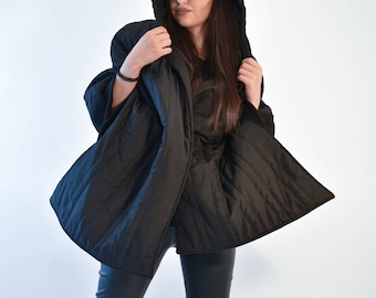 May include: A black quilted jacket with a hood and a black baseball cap. The jacket is open and the person is wearing black pants and black sneakers.