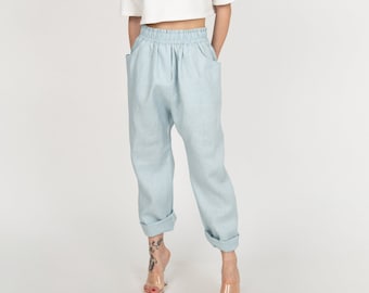 May include: A woman wearing a white cropped top and light blue denim pants with a drawstring waist. She is wearing clear heeled sandals.