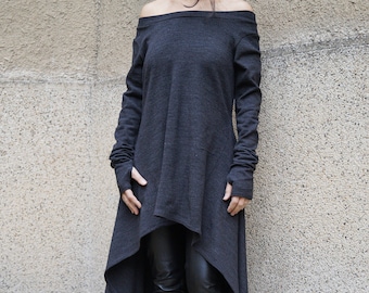 May include: A long, gray, off-the-shoulder sweater with long sleeves and thumb holes. The sweater has a high-low hemline and is styled with black leggings and black knee-high boots.