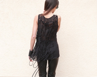 May include: A woman wearing a black sheer top with a unique knotted design and black leather pants. She is wearing black heeled boots.