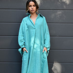 May include: A long, flowing turquoise dress with a collared neckline and long sleeves. The dress has pockets and a relaxed fit, suitable for casual wear. The fabric appears to be a lightweight linen or similar material.