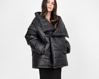 May include: A black puffer jacket with a large, asymmetrical collar. The jacket is quilted and has a shiny finish. The model is wearing a black skirt and clear heels.