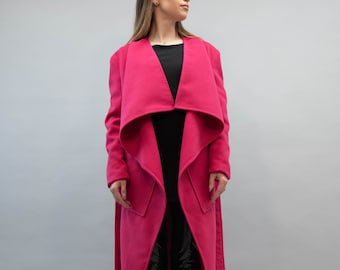 Könnte beinhalten: Ein langer, rosa Wickelmantel mit einem breiten Kragen und einem Gürtel. Der Mantel ist aus einem weichen, warmen Stoff gefertigt und hat eine lockere Passform.
