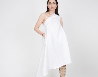 May include: A white one-shoulder dress with a flowing asymmetrical hemline. The dress is made of a lightweight fabric and is paired with beige cut-out boots.