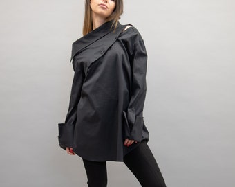 Könnte beinhalten: Ein schwarzes, langärmliges Hemd mit asymmetrischem Kragen und einem einzigen Knopfverschluss. Das Hemd wird mit einer schwarzen Hose und schwarzen Schuhen mit Absatz getragen.