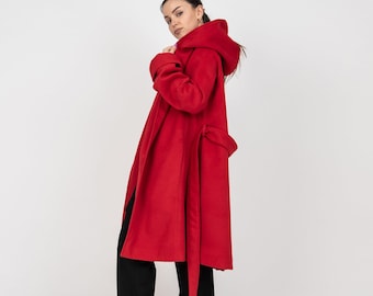 Könnte beinhalten: Ein leuchtend roter Mantel aus Wollmischgewebe mit großer Kapuze, langen Ärmeln und einem passenden Bindegürtel in der Taille. Der Mantel wird über einer schwarzen Hose getragen und mit roten Schuhen mit spitzer Zehenpartie kombiniert.
