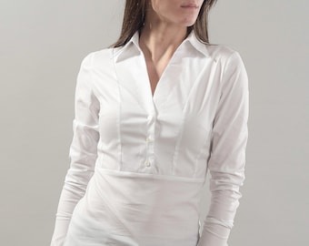 May include: A white long-sleeved button-down shirt with a v-neck collar and a fitted waist. The shirt is worn by a person wearing black pants and sunglasses.
