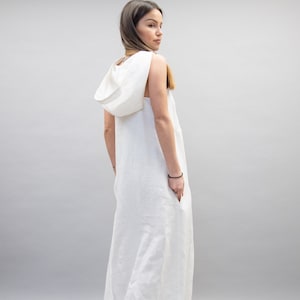 May include: A white linen maxi dress with a hood. The dress is sleeveless and has a relaxed fit.