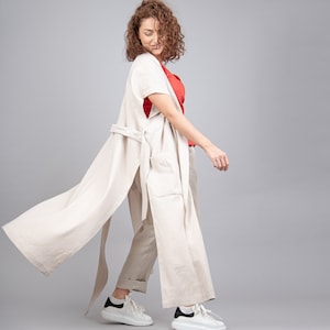 Può includere: Una donna indossa un lungo duster di lino beige chiaro con cintura, una maglietta rossa e scarpe da ginnastica bianche.